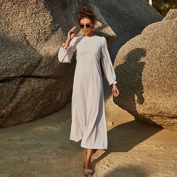 Model in cream modest swim dress walking along a sunny shoreline