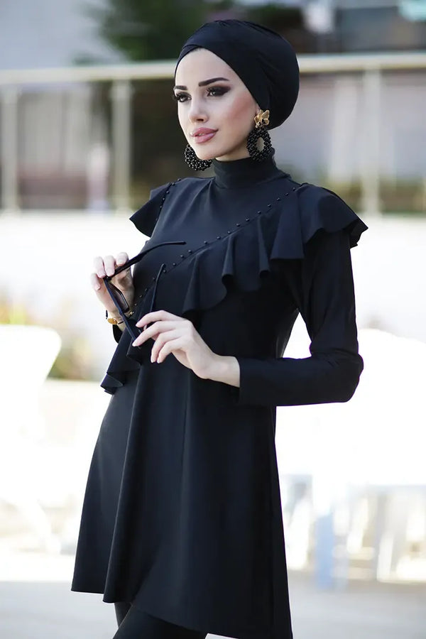 Model wearing black modest bathing suit with ruffle front and matching swim cap
