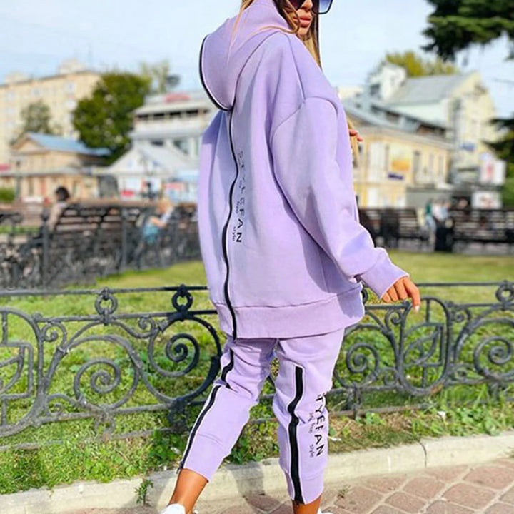 Person wearing a lavender tracksuit with '' branding in an outdoor setting.