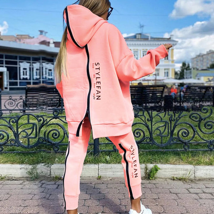 Person wearing a pink tracksuit with '' branding in an outdoor setting.