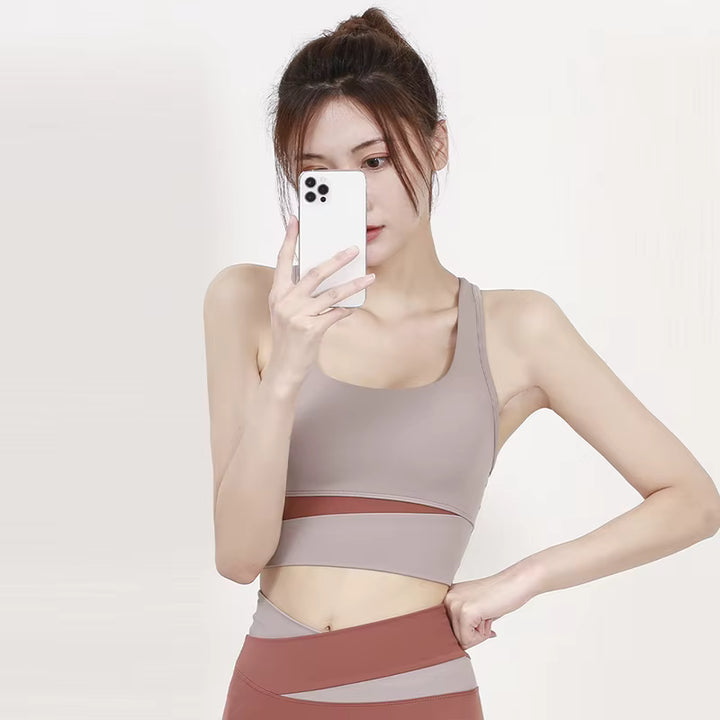 Woman taking a mirror selfie wearing a beige sports bra and leggings on a plain background
