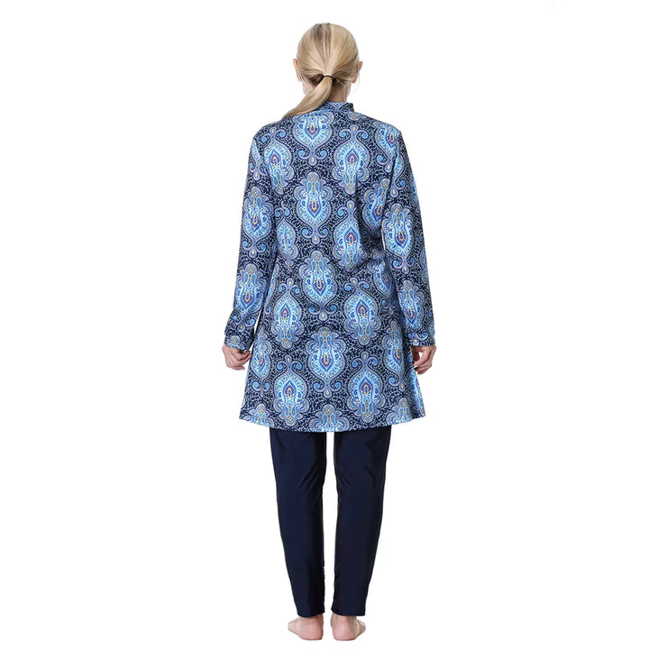 Woman wearing a blue patterned modest swimwear top and dark pants on a white background