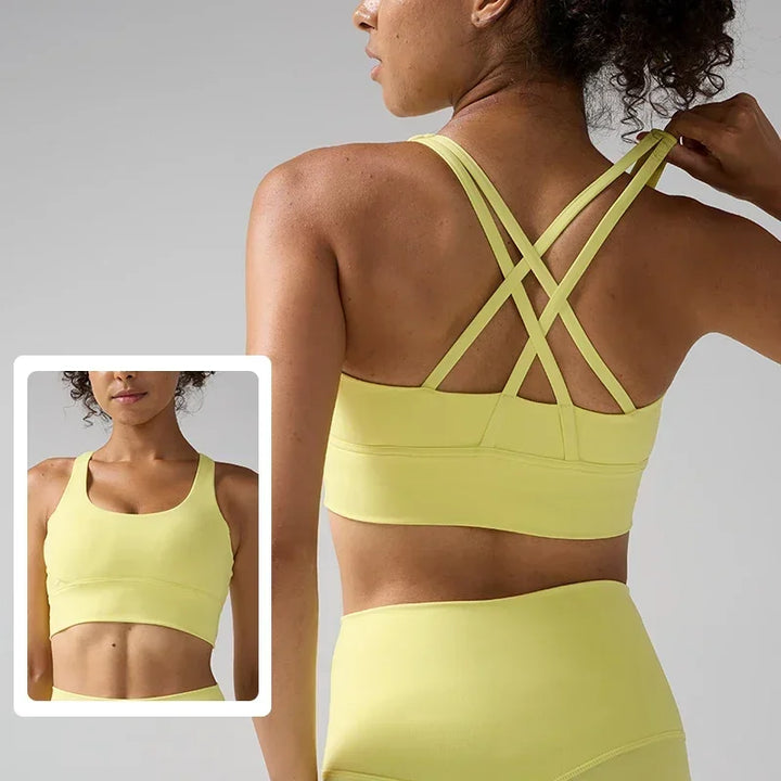 Woman wearing a yellow sports bra and leggings with criss-cross back design, on a gray background.